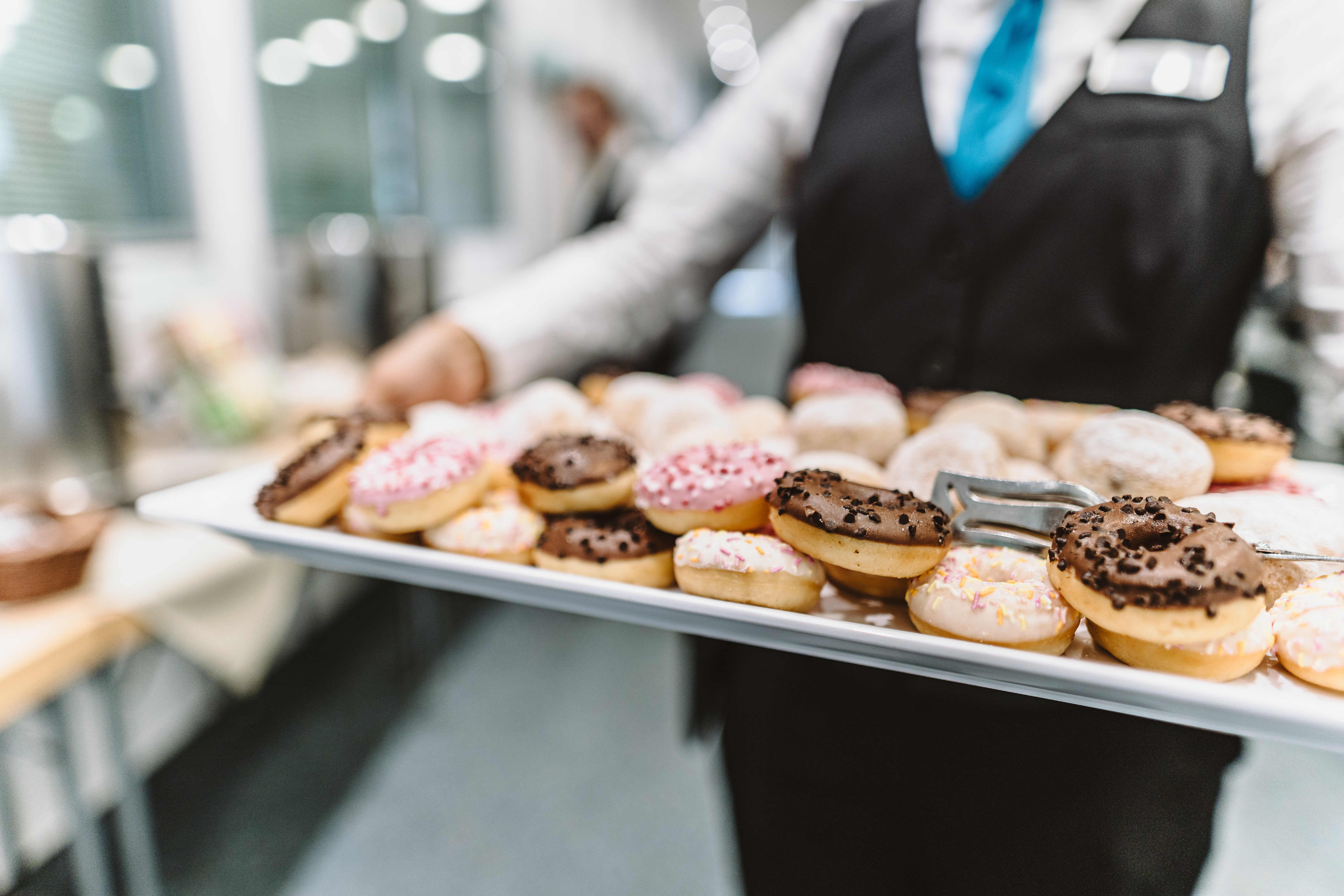 [Translate to Englisch:] Eine Servicekraft hält eine Platte mit Donuts in verschiedenen Geschmacksrichtungen.
