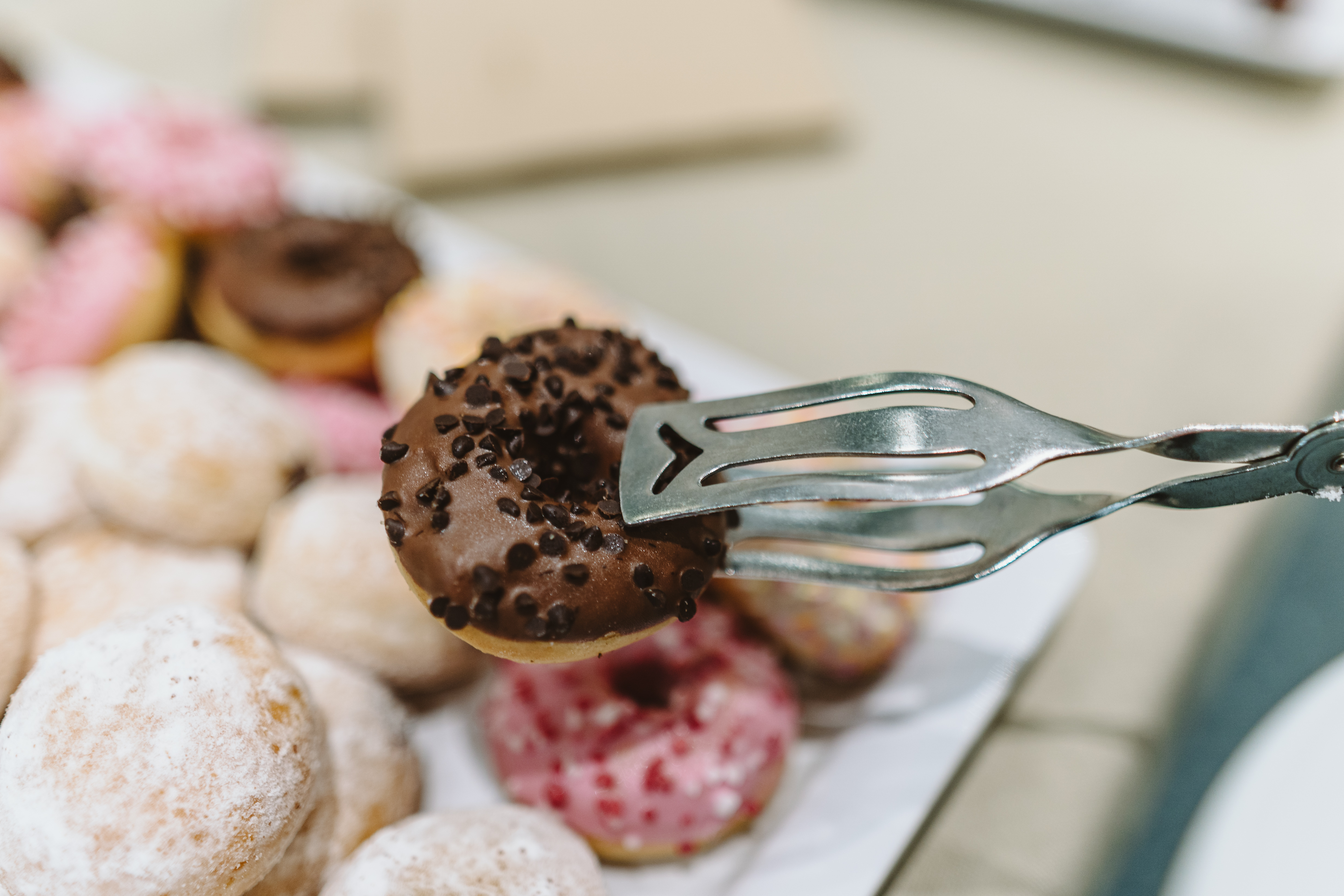 Eine Gebäckplatte mit Schokodonut, Erdbeerdonut und Berliner. Ein Tagungsgast nimmt sich mit einer Zange ein Gebäckstück.