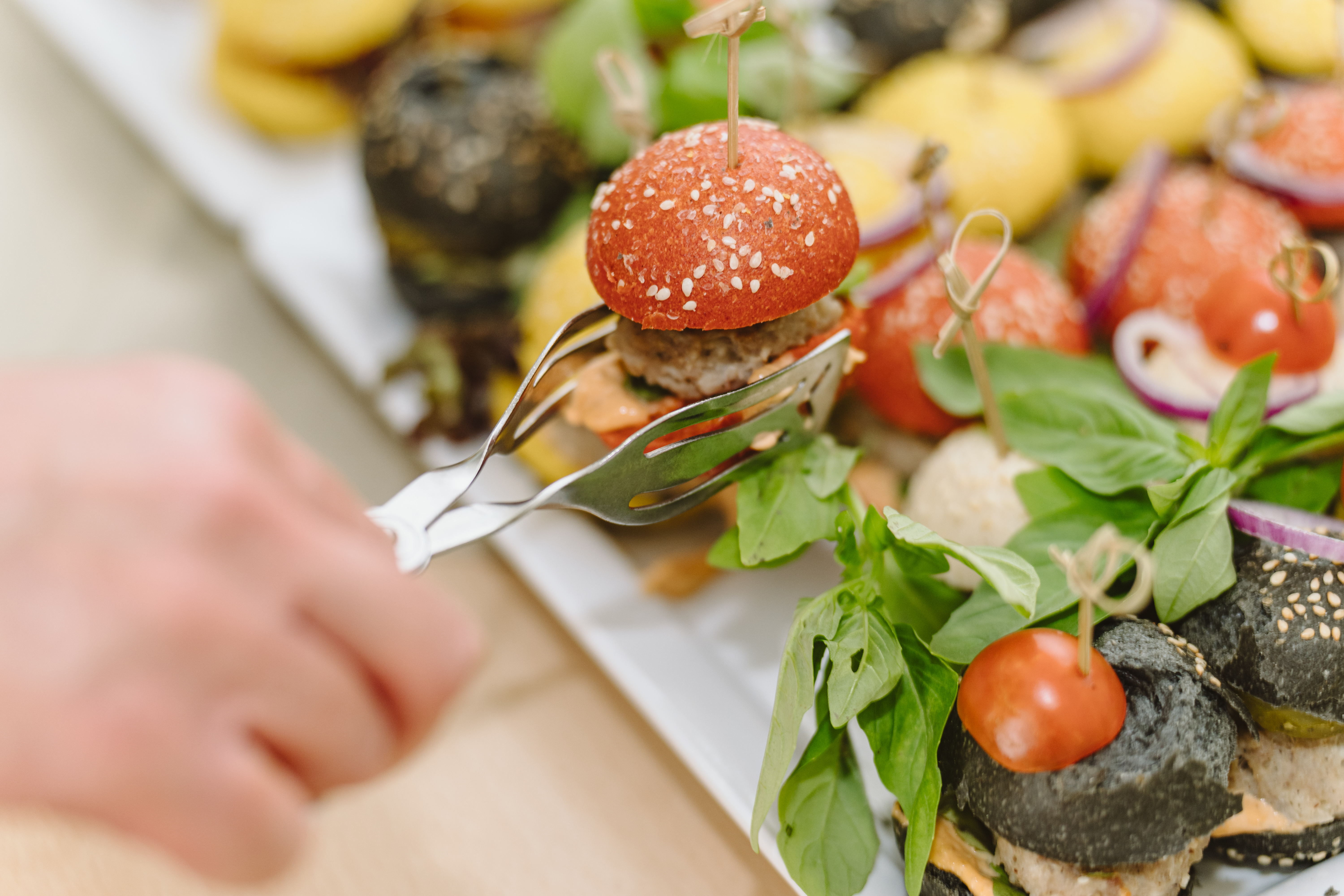 Ein Tagungsgast nimmt sich einen bunten Mini-Burger vom Buffet. Im Hintergrund sind weitere Burger zu sehen.
