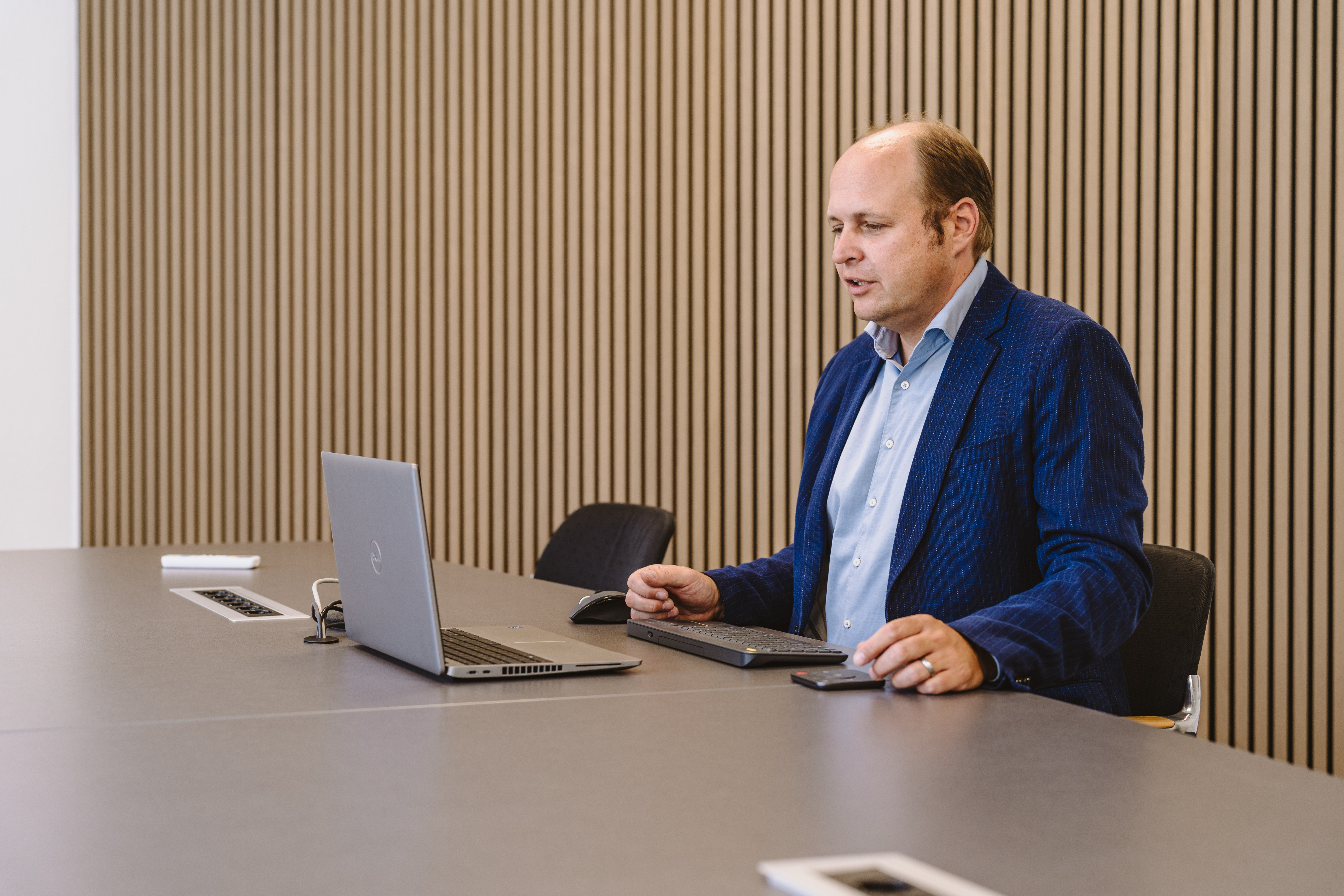 Ein Mann sitzt in einem Tagungsraum am Laptop und wirkt nachdenklich.